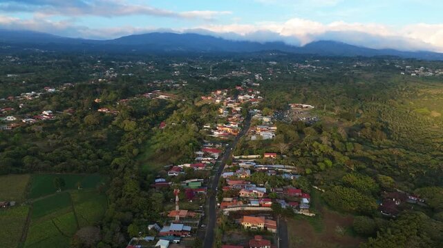 Aerial pull-back shot over a winding mountain road and residential houses surrounded by lush tropical forest in San Rafael, Heredia, Costa Rica at sunset