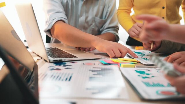 A diverse team collaborates on a project in a modern office, using a laptop and colorful documents to analyze data and discuss strategies for success. SACTR