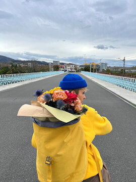 Person carrying colorful flowers on a bridge in an urban setting