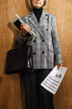 Mature businesswoman holding documents, notebook, and leather bag 