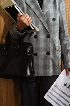 Woman in checkered blazer holding documents, notebook and leather bag