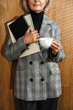 Mature woman in grey blazer holding cup and notebooks