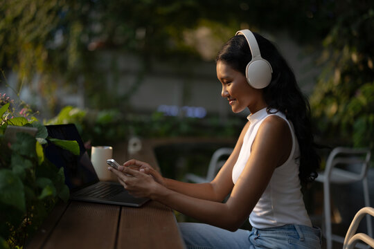 Young Woman Wearing Headphones Working on Laptop Outdoors