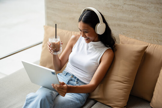 Woman With Headphones Relaxing On Sofa, Using Tablet