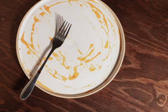Dirty plate with orange sauce and fork on wooden surface
