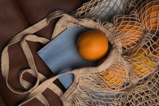 Top view of oranges in mesh bag with book on brown leather
