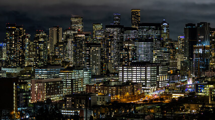 Night view of downtown Seattle showing dense illuminated skyscrapers, busy streets, and glowing windows under dramatic dark clouds. Ideal for business, technology, and urban lifestyle themes.