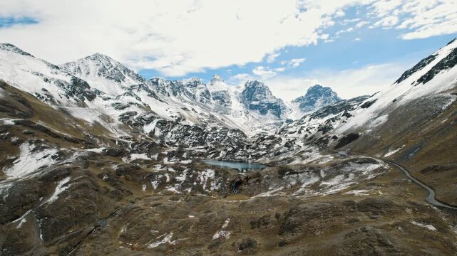 Breathtaking drone footage of the rugged, snow-dusted Andes mountains at Pico Austria. A remote glacial lake sits nestled among the peaks under a clear blue sky in the Bolivian Altiplano.