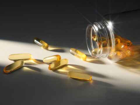 Golden capsules spill from a clear bottle, catching the sunlight