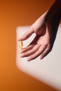 A hand holds a single, golden capsule against an orange backdrop