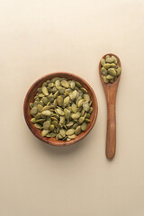 Green Pumpkin seeds in a wooden bowl placed on a beige background.