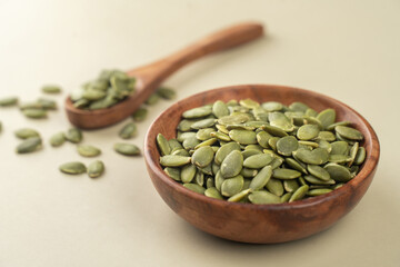 Green Pumpkin seeds in a wooden bowl placed on a beige background.