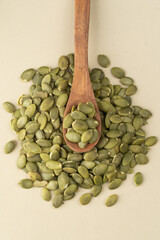 Green Pumpkin seeds in a wooden spoon placed on a beige background.