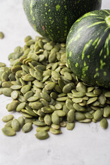 Green Pumpkin seeds in a wooden bowl, along with green baby pumpkin, placed on a textured background.
