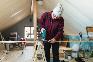 Active Senior Woman Cutting Wood with Jigsaw in Attic