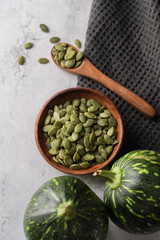 Green Pumpkin seeds in a wooden bowl, along with green baby pumpkin, placed on a textured background.