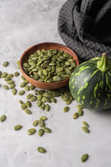 Green Pumpkin seeds in a wooden bowl, along with green baby pumpkin, placed on a textured background.