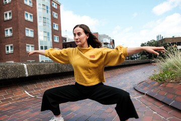 Young woman dancing wearing yellow sweater and black pants in urban setting