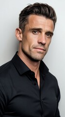 Confident man with stylish hair wearing a black shirt poses against a light background, showcasing a modern and professional appearance with a captivating expression