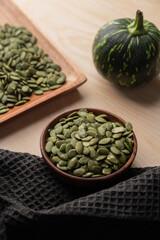 Green Pumpkin seeds in a wooden bowl, along with green baby pumpkin, placed on a textured background.