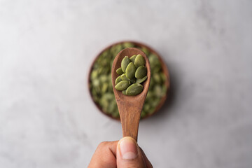 Green Pumpkin seeds in a wooden spoon placed on a textured background.