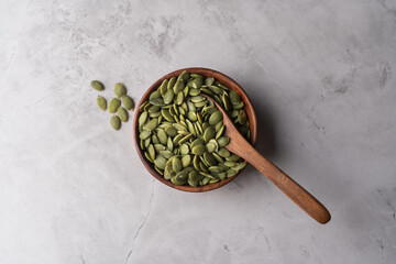Green Pumpkin seeds in a wooden bowl placed on a textured background.