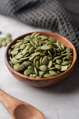 Green Pumpkin seeds in a wooden bowl placed on a textured background.