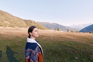 Woman portrait in jacket standing in mountain meadow, looking into distance across landscape and nature. Outdoors scene with clear sky, rolling hills and peaceful rural atmosphere. © SHOTPRIME STUDIO