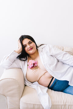 A curvy woman is sitting on a couch with flowers on her chest.