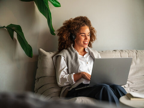 Woman Relaxing on Couch with Laptop and Headphones for Online Meeting