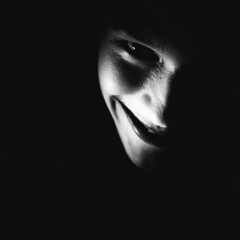 Mysterious figure with a sinister smile illuminated by soft light in a dark environment, creating an eerie atmosphere that evokes intrigue and suspenseful emotions