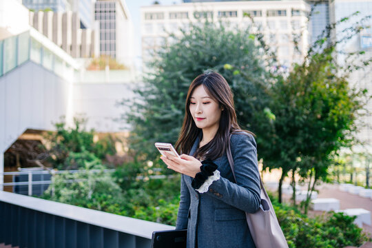 Japanese businesswoman walking outdoors checking smartphone