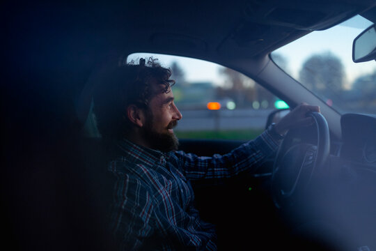 Smiling man driving at dusk, enjoying a peaceful evening in the city
