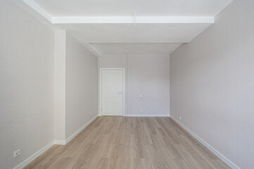 minimalist room with light wooden flooring, off-white walls, white ceiling, recessed design, white door, and electrical outlets — clean, bright, uncluttered space