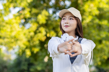 Asian woman wearing wireless headphones, smiling while relaxing in a park after workout and stretching, enjoying music and peaceful outdoor moment of contentment and well-being.