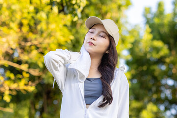 Asian woman wearing wireless headphones, smiling while relaxing in a park after workout and stretching, enjoying music and peaceful outdoor moment of contentment and well-being.