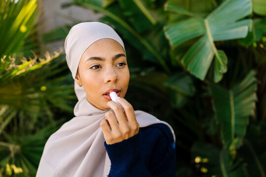 Muslim woman applying lip balm for self care