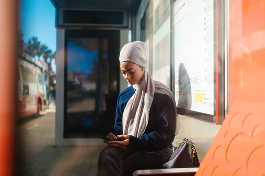 Young woman with hijab using smartphone at bus stop