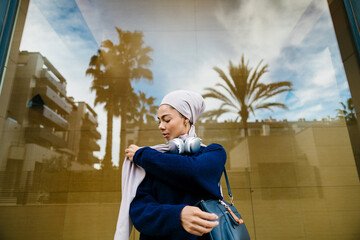 Stylish woman wearing hijab adjusting scarf in city