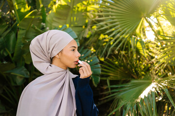 Muslim woman applying lip balm outdoors