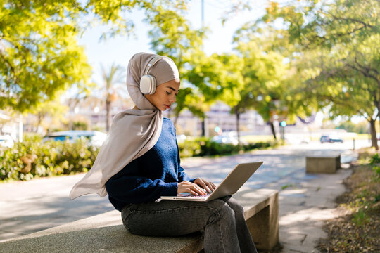 Muslim woman working remotely with laptop in park