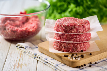Raw beef burger patties one above other on a white table.