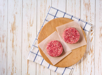 Raw minced beef patties for burgers on a white table, top view.