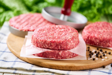 Raw ground beef burger patties separated by parchment paper on a white table, selective focus.