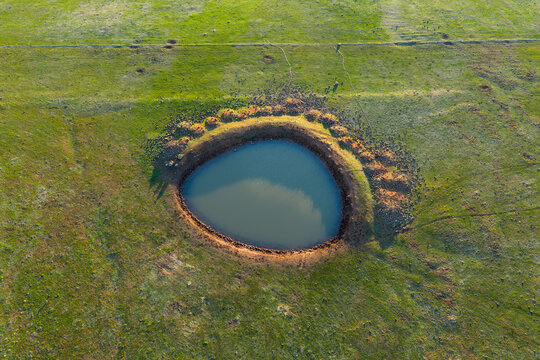 Farm dam the shape of an eye in a green field