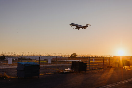 Airplane landing at sunset near fenced runway