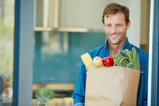 Portrait, paper bag and happy man with groceries in home, fresh vegetables and organic ingredients purchase. Smile, healthy food and person with produce delivery, sustainable consumer and vegan diet - Powered by Adobe