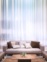 Modern bright living room interior with a beige sofa, wooden coffee table, and white sheer curtains. Minimalist cozy home decor for real estate and lifestyle concepts