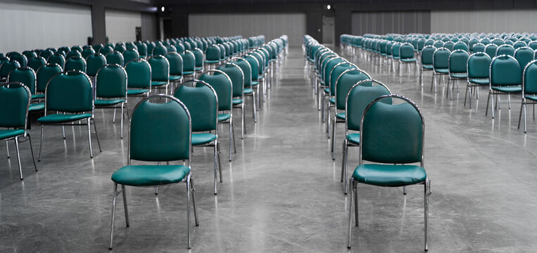 Rows of teal chairs arranged in a large conference hall for a seminar or business event. Professional indoor venue setup with symmetric seating and spacious interior