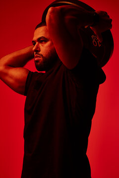 Muscular athlete lifting weight against a red backdrop